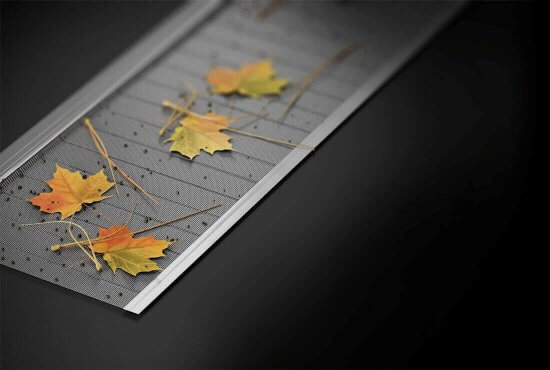 Close-up of a metal gutter guard with several yellow and orange autumn leaves and pine needles resting on top, against a dark background.