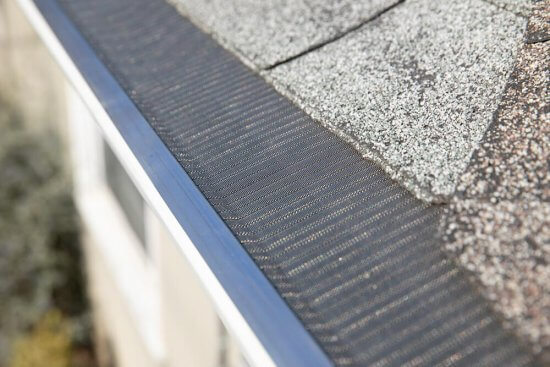 Close-up view of a house roof with asphalt shingles and a metal mesh gutter guard installed along the edge to prevent debris from entering the gutter.