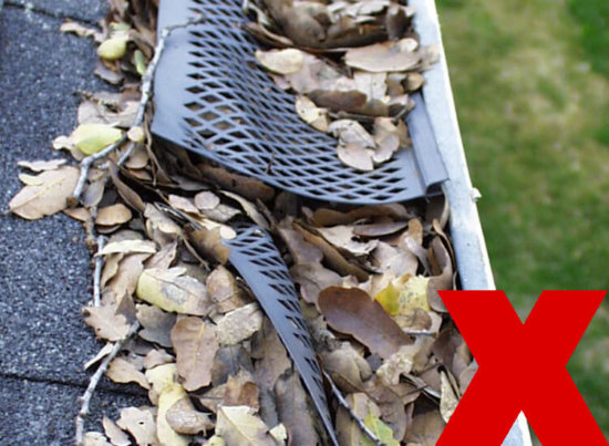 A gutter filled with dry leaves and debris, covered by a broken plastic mesh guard. A large red X symbol is overlaid in the bottom right corner, indicating something is wrong.
