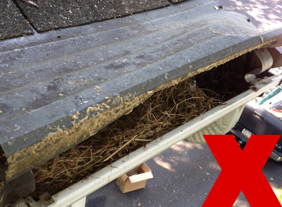 A house gutter filled with dried leaves and debris, indicating it is clogged. There is a large red X in the bottom right corner, signifying this is incorrect or undesirable.
