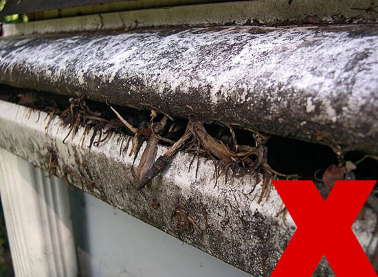 A dirty, clogged gutter filled with leaves and debris, with a large red X in the bottom right corner indicating something is wrong.
