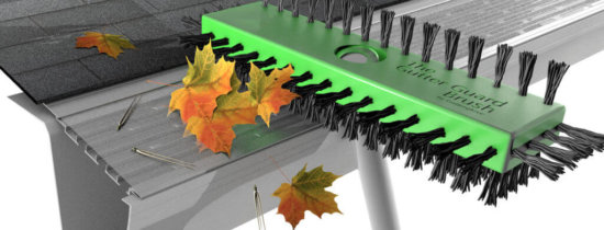 A green gutter guard brush with black bristles cleans a gutter filled with leaves and pine needles, next to a roof with shingles. Some leaves rest on the gutter guard.
