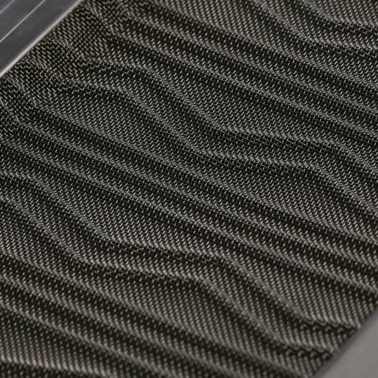 Close-up of a black air filter with a tightly woven mesh and diagonal zigzag pattern, framed by a dark border. The texture and pattern of the filter material are clearly visible.