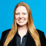 A woman with long straight blonde hair smiles at the camera. She wears a dark blazer over a dark shirt and stands in front of a bright blue background, representing Gutterglove, a leading gutter guard manufacturer known for stainless steel micro-mesh.